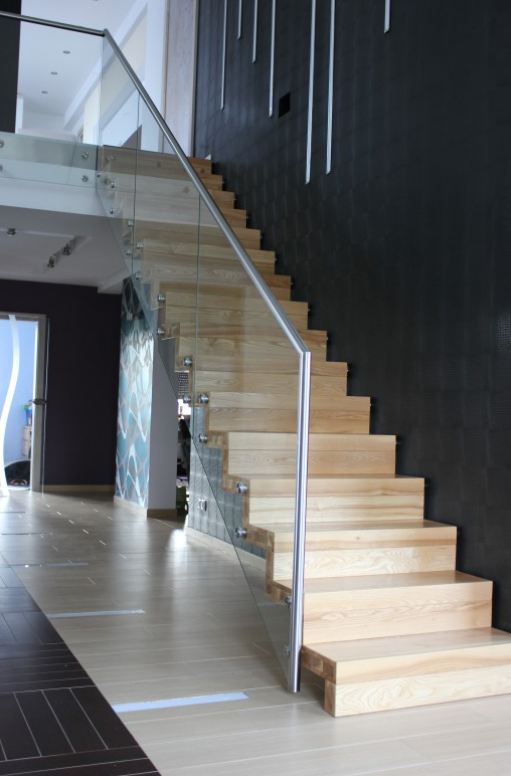 Drewniane schody dywanowe z balustradą szklaną oraz metalową poręczą