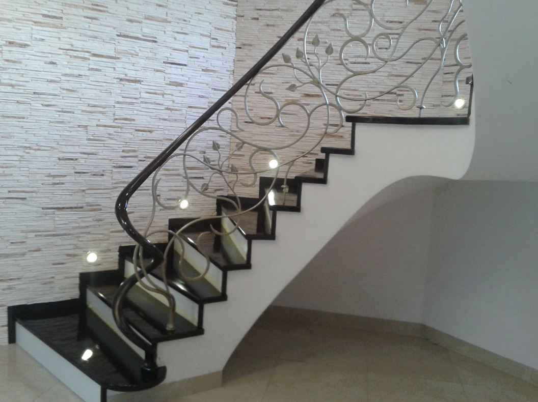 Drewniane schody z metalową balustradą z motywem roślinnym i drewnianymi poręczami